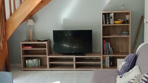 Ein Wohnzimmer mit einer Holztreppe, einem Flachbildfernseher, einem Bücherregal und einem Essbereich mit Tisch und Stühlen.