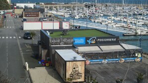 Ein Yachthafen mit vertäuten Booten, ein Restaurant namens 'Cabane du Pecheur' und Blick auf das Meer.