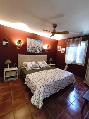 Ein Schlafzimmer mit Bett, Nachttischen, Deckenventilator und einem Fenster mit Vorhängen.