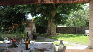 Un espace de restauration en plein air avec une table dressée pour deux personnes, entouré de verdure et bordé d’un mur en pierre.