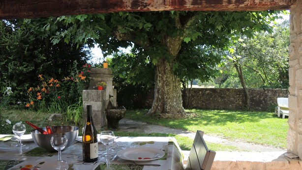 Un espace de restauration en plein air avec une table dressée pour deux personnes, entouré de verdure et bordé d’un mur en pierre.