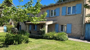 Une maison à deux étages avec une façade en pierre, des volets bleus et un petit porche.