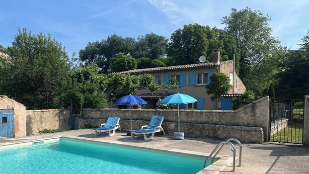 Une piscine entourée de murs de pierre et d’arbres, avec des chaises longues et des parasols.