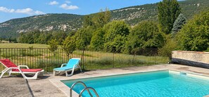 En swimmingpool med to liggestole, en rød og en blå, samt et metalhegn.