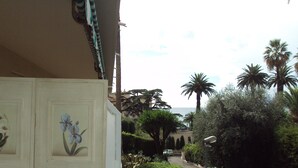 A narrow street with parked cars, palm trees, and a building with a white facade and floral decorations. -  Beautiful Cannes Apartment (Cannes)