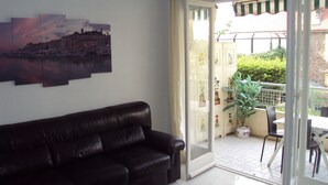 A living room with a black leather sofa, a cityscape painting, and a view of a balcony with outdoor furniture. -  Beautiful Cannes Apartment (Cannes)