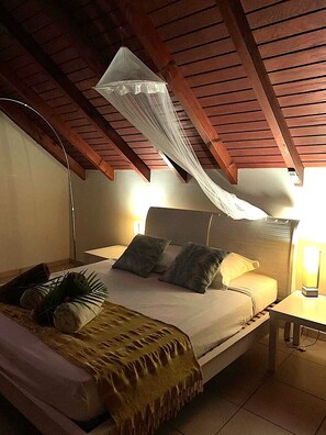 A bedroom with a bed, bedside lamps, a canopy, and a bedside plant. - Comfortable villa, swimming pool, tropical garden, near beach st Anne, 8 pers (Sainte Anne)