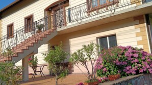 Een tweelaags huis met een balkon, een trap en een stenen muur met plantenpotten.