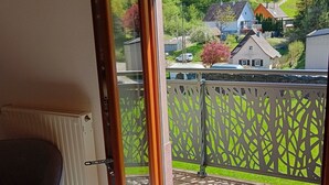 Een kamer met een schuifglazen deur die leidt naar een balkon met uitzicht op huizen en bomen.