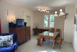 Un comedor con una mesa y sillas de madera, un televisor sobre un mueble bajo, y un candelabro sobre una mesita auxiliar.