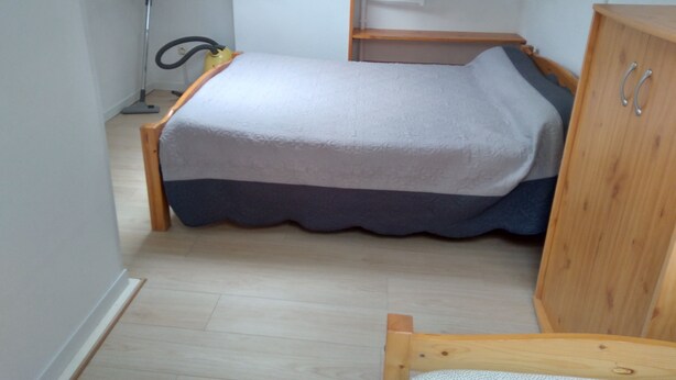 A small, compact bedroom with a bed, a wooden wardrobe, and a vacuum cleaner. - Garden floor with mezzanine close to all amenities and the center (Portiragnes)