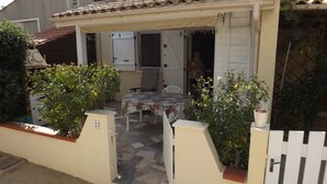 A covered patio with a table and chairs, surrounded by potted plants and a white gate. - Garden floor with mezzanine close to all amenities and the center (Portiragnes)