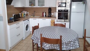 A compact kitchen with white cabinets, a washing machine, a microwave, an oven, and a refrigerator. - Garden floor with mezzanine close to all amenities and the center (Portiragnes)