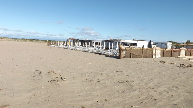 A beach with rows of white sun loungers and umbrellas, a fenced area with buildings, and a clear sky. - Garden floor with mezzanine close to all amenities and the center (Portiragnes)