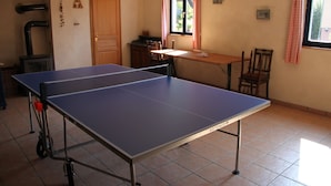 Ein Zimmer mit einem Ping-Pong-Tisch, einer Holztür, einem Fenster mit roten und weißen Karottenvorhängen und einem Fliesenboden.