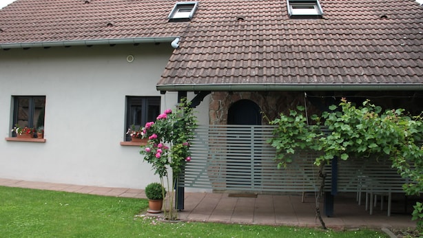 Ein Haus mit einem Ziegeldach, einer Veranda und einem kleinen Garten mit Blumen und einem Topfpflanzen.
