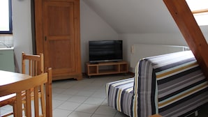 Ein kleiner, gemütlicher Raum mit einem Holzespeisetisch, einer gestreiften Couch, einem Fernseher auf einem Holzschrank und einem Holzschrank.