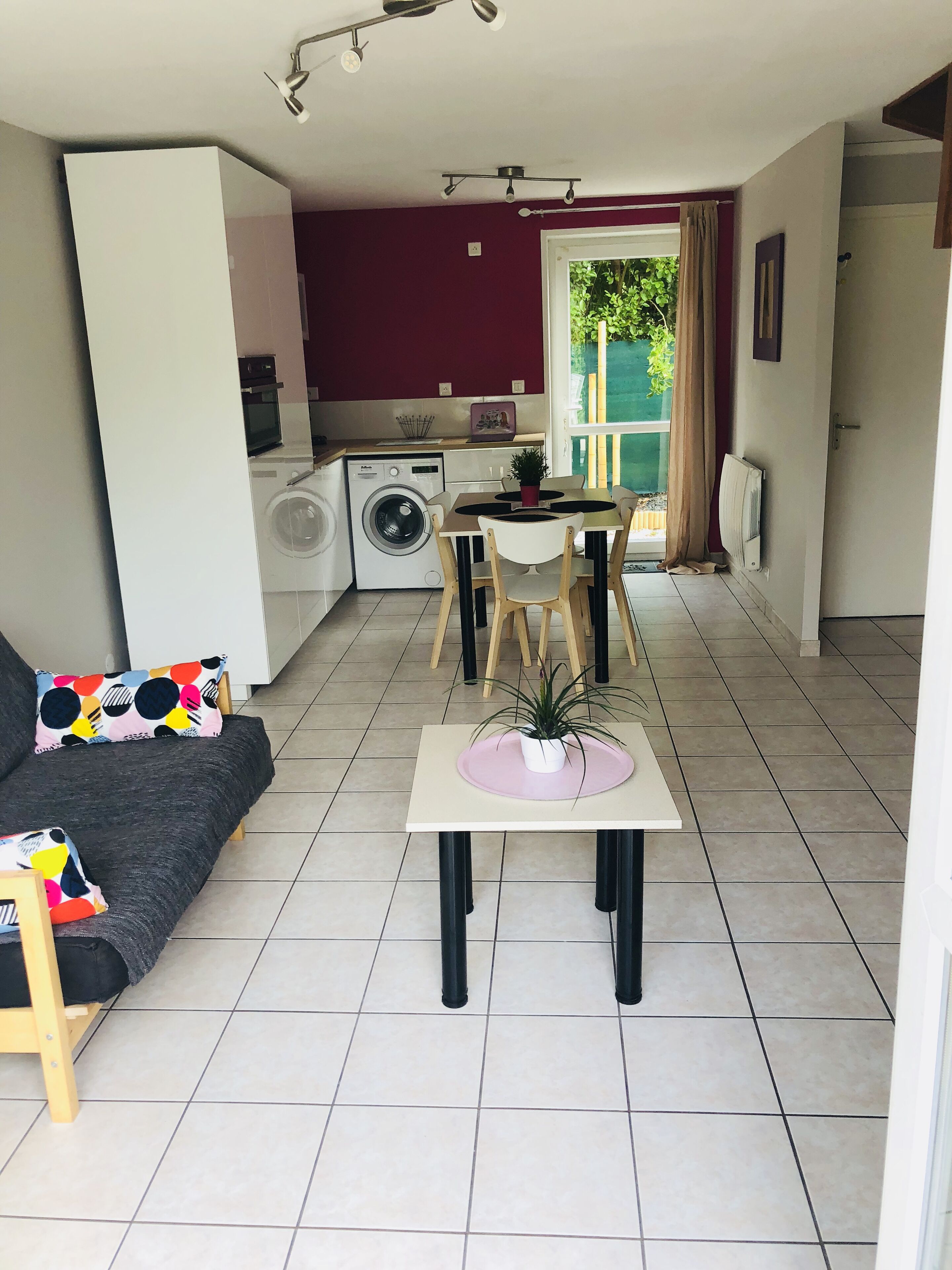 En kompakt opholdsstue med sofa, spisebord, vaskemaskine og et lille køkken.
