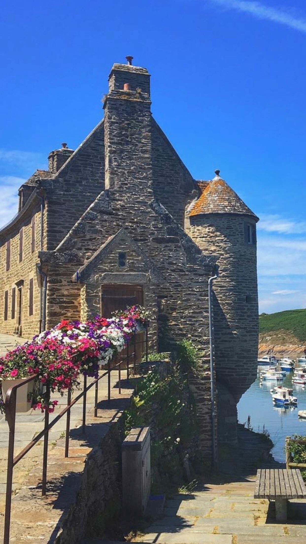 Ein Steinhaus mit einem markanten Turm und einem kleinen Balkon mit Blumen.