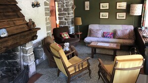 Un salón acogedor con chimenea de piedra, muebles de madera y una pared verde decorada con cuadros.