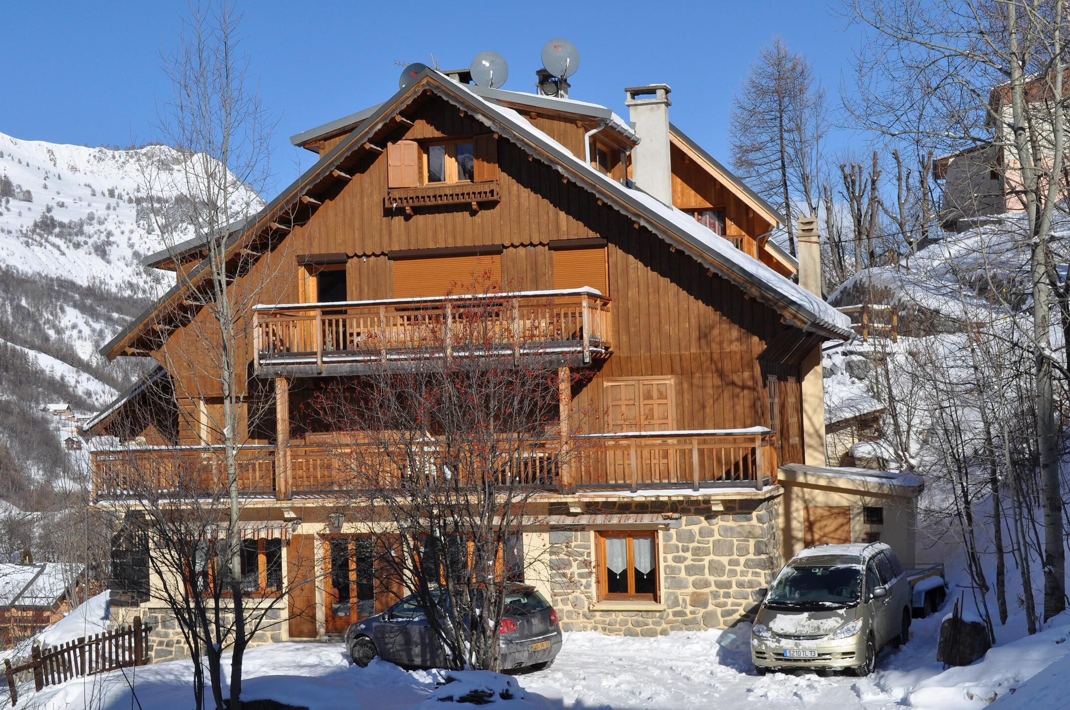A wooden chalet with a balcony, stone foundation, and snow-covered surroundings.