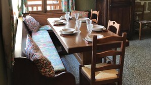 Un comedor con una mesa de madera dispuesta para cuatro personas, un banco con cojines estampados y una pared de piedra al fondo.