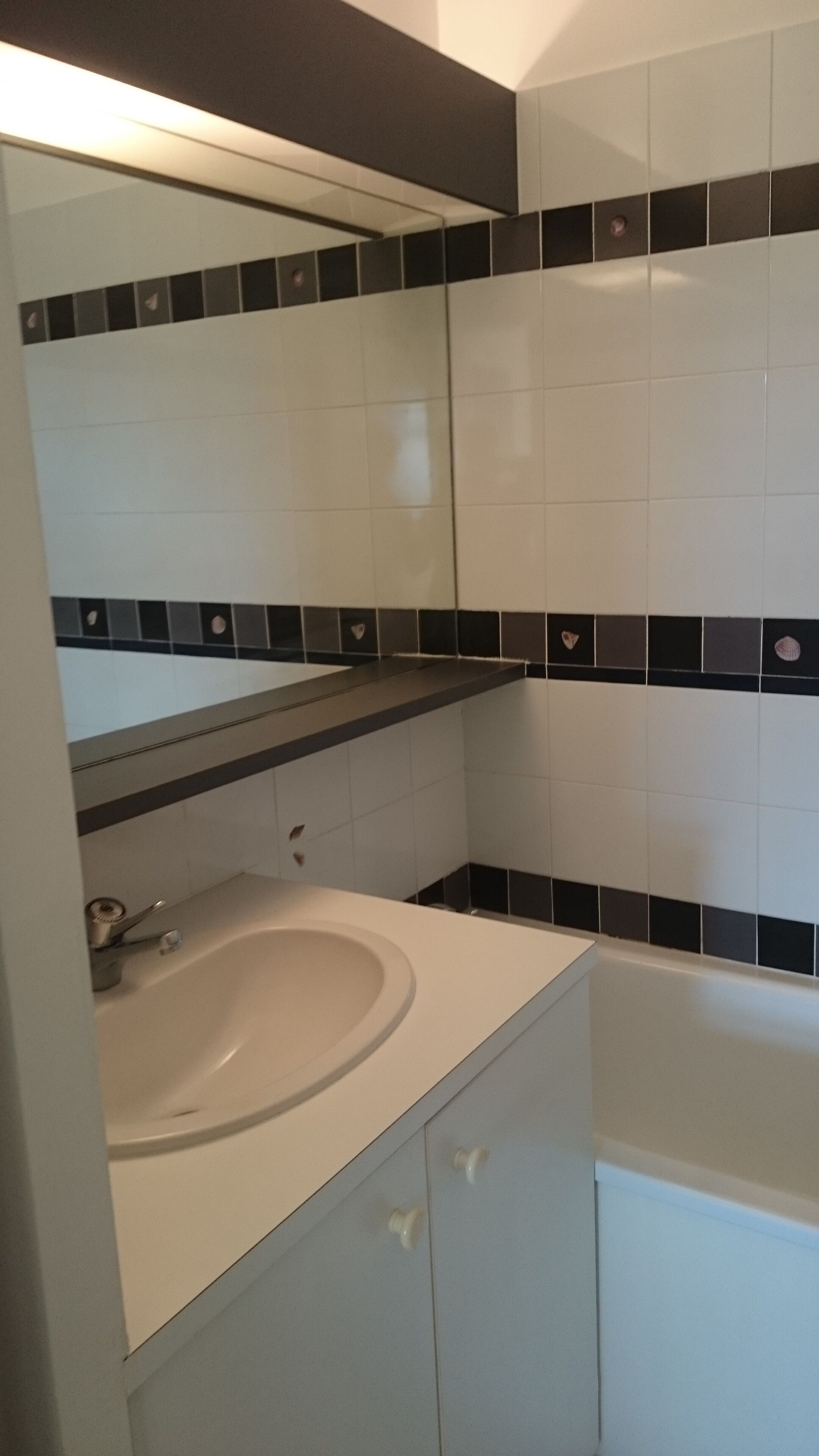 A bathroom with a white sink, a mirror, and black and white tiled walls.