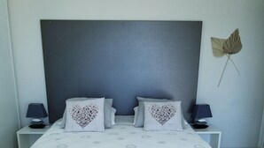 Ett modernt sovrum med en stor säng, två sängbord, en grå pall och en väggbeklädnad med intressant struktur bakom sängen.