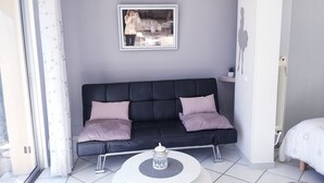 Ett modernt vardagsrum med en svart soffa, två kuddar, ett vitt soffbord och ett inramat konstverk på väggen.