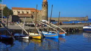 Un pueblo costero con una torre de piedra histórica, un muro fortificado y varios botes de colores amarrados en el puerto.