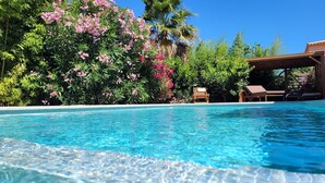 Una piscina azul cristalina con sillones de descanso y un pérgola de madera.