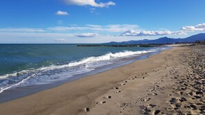 Una playa con huellas que conducen al agua, cielo despejado y montañas a lo lejos.