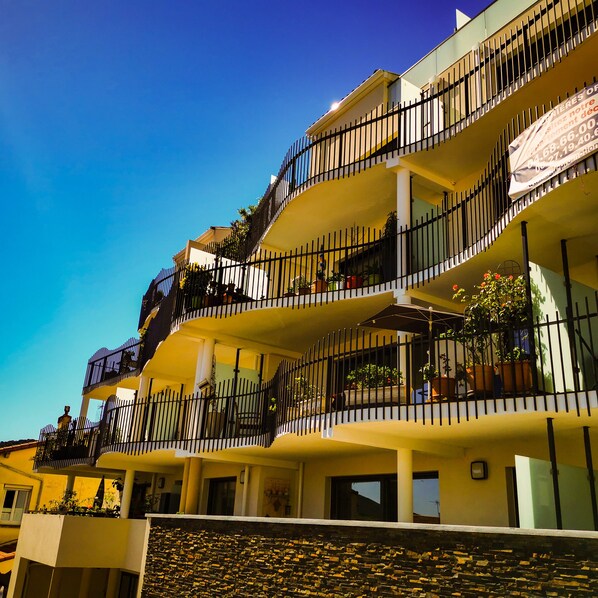 Un hotel de varios pisos con balcones, mobiliario exterior y plantas en macetas.