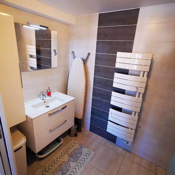 Un baño con lavamanos blanco, espejo y toallero.