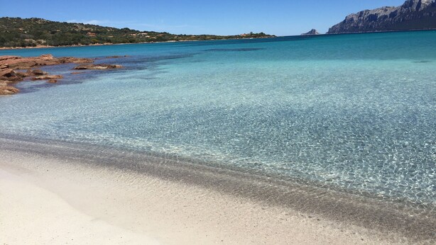 Una spiaggia con acque cristalline color turchese, una battigia sabbiosa e affioramenti rocciosi.