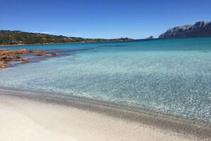 Een strand met helder turquoise water, een zandstrand en rotsachtige rotsformaties.