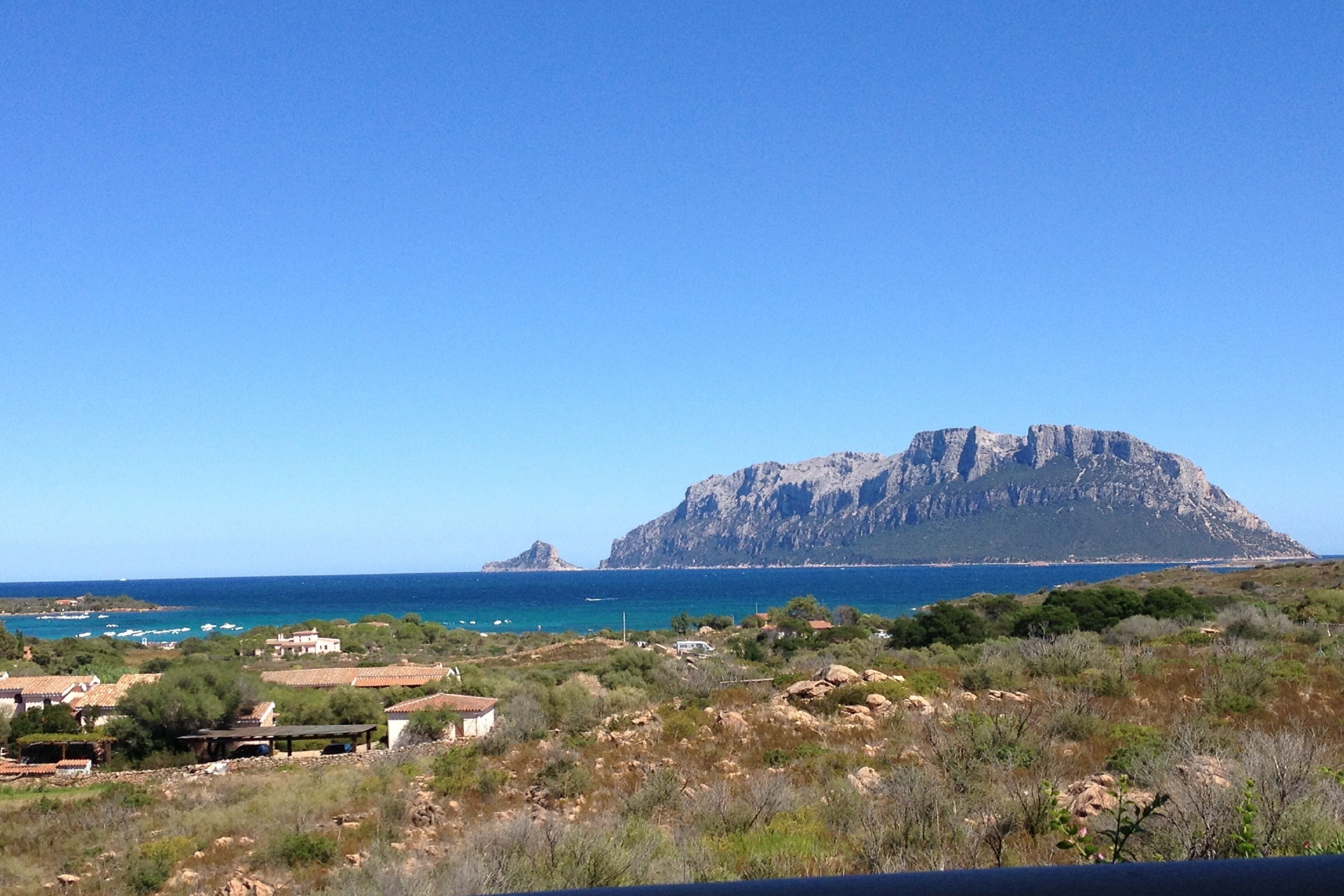 Un paisaje costero con una colina rocosa destacada, cielo azul despejado y vista al mar.