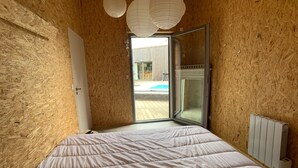 Ett sovrum med en stor säng, träväggar, en skjutdörr i glas som leder ut till ett utomhusområde och ett element på väggen.