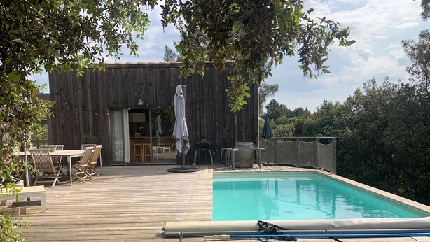 Ett trädäck med en pool, utomhusmöbler och en byggnad med en skjutdörr.