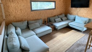 Ett mysigt vardagsrum med en hörnsoffa, en platt-TV som är monterad på väggen och ett fönster som släpper in naturligt ljus.