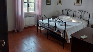 Ein Schlafzimmer mit einem Bett, einem Nachttisch, einem Fenster mit Vorhängen und gerahmten Bildern an der Wand.