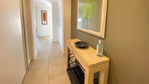 Un couloir avec une console en bois, une œuvre d’art encadrée et une bouteille de gel hydroalcoolique.