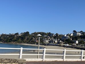A coastal view with a white railing, a beach, and buildings in the background.