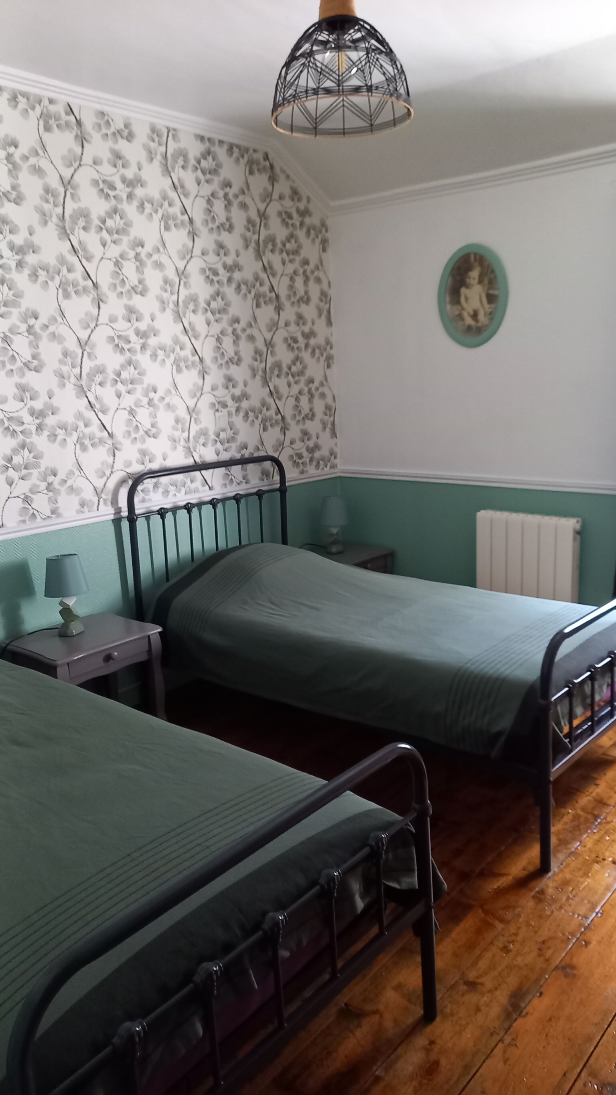 A room with two beds, a wall with floral wallpaper, a round picture frame, and a radiator.