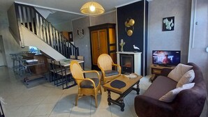 Een woonkamer met een bank, stoelen, een televisie, een open haard en een trap.