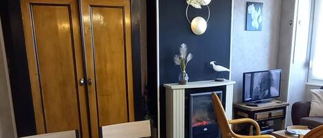 A dining area with a wooden table and chairs, a TV, and a fireplace.