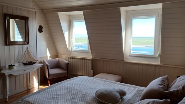 Een slaapkamer met een bed, een stoel, een klein tafeltje, een raam en een radiator.