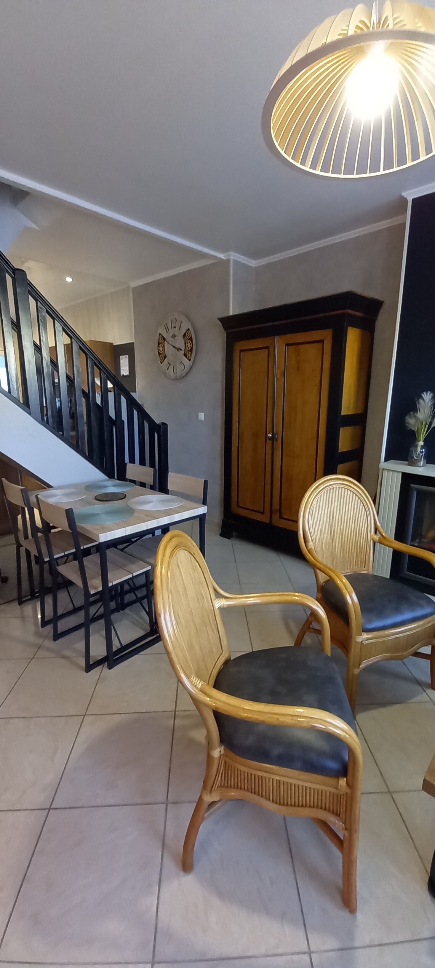 A dining area with a table and chairs, a clock on the wall, and a staircase in the background.