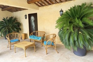 A patio area with wicker furniture, a large potted plant, and a wall-mounted lamp. - Charming furnished apartment in Mas, UzËs, pool, 656 yards away from town centre (Uzès)