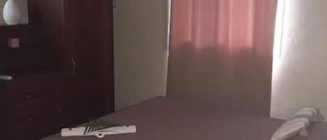 A bedroom with a bed, a wardrobe, an air conditioner, and a curtain.